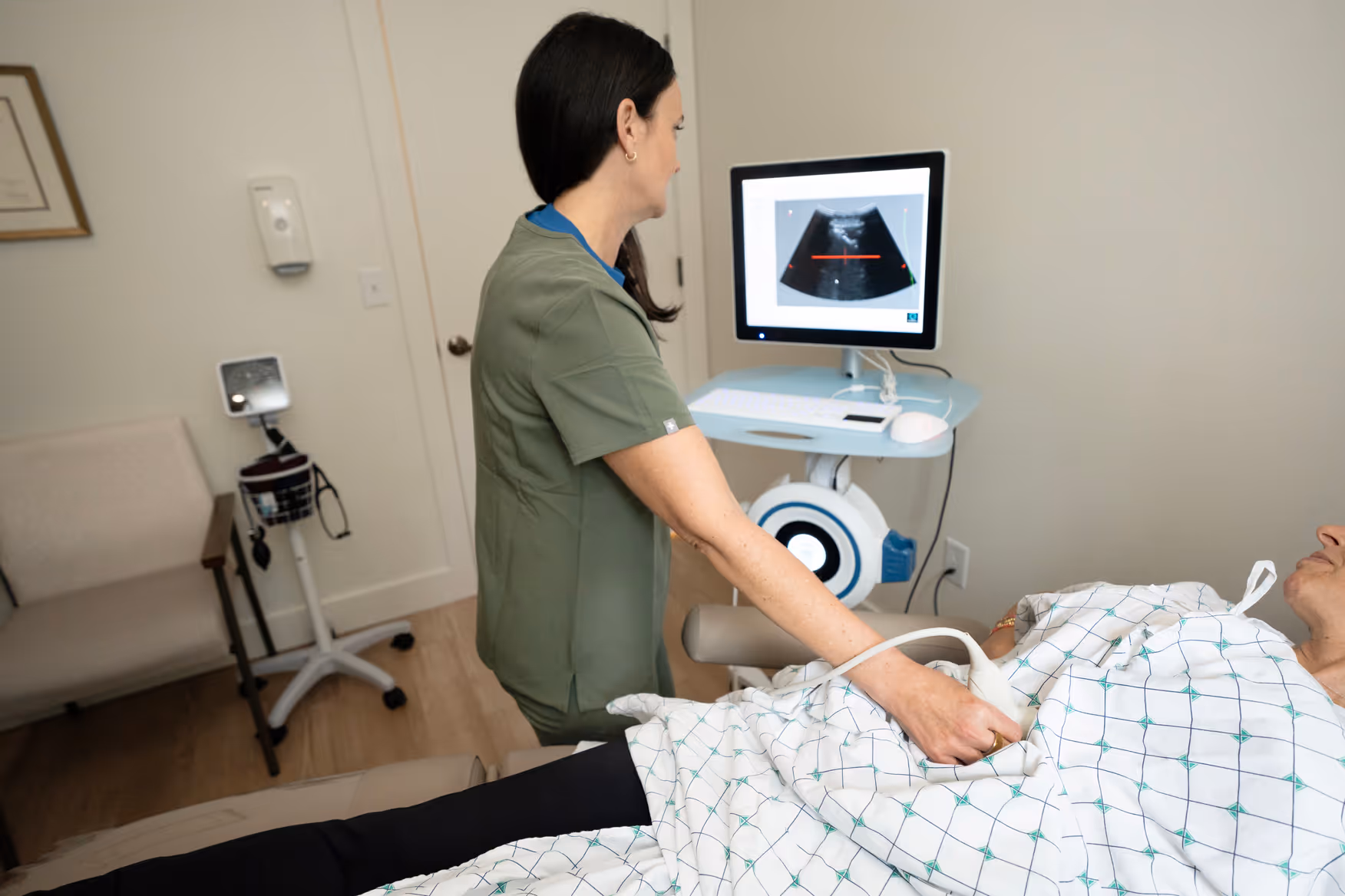 A sonographer performing an echocardiogram on a patient lying on an exam table, the heart image on the screen