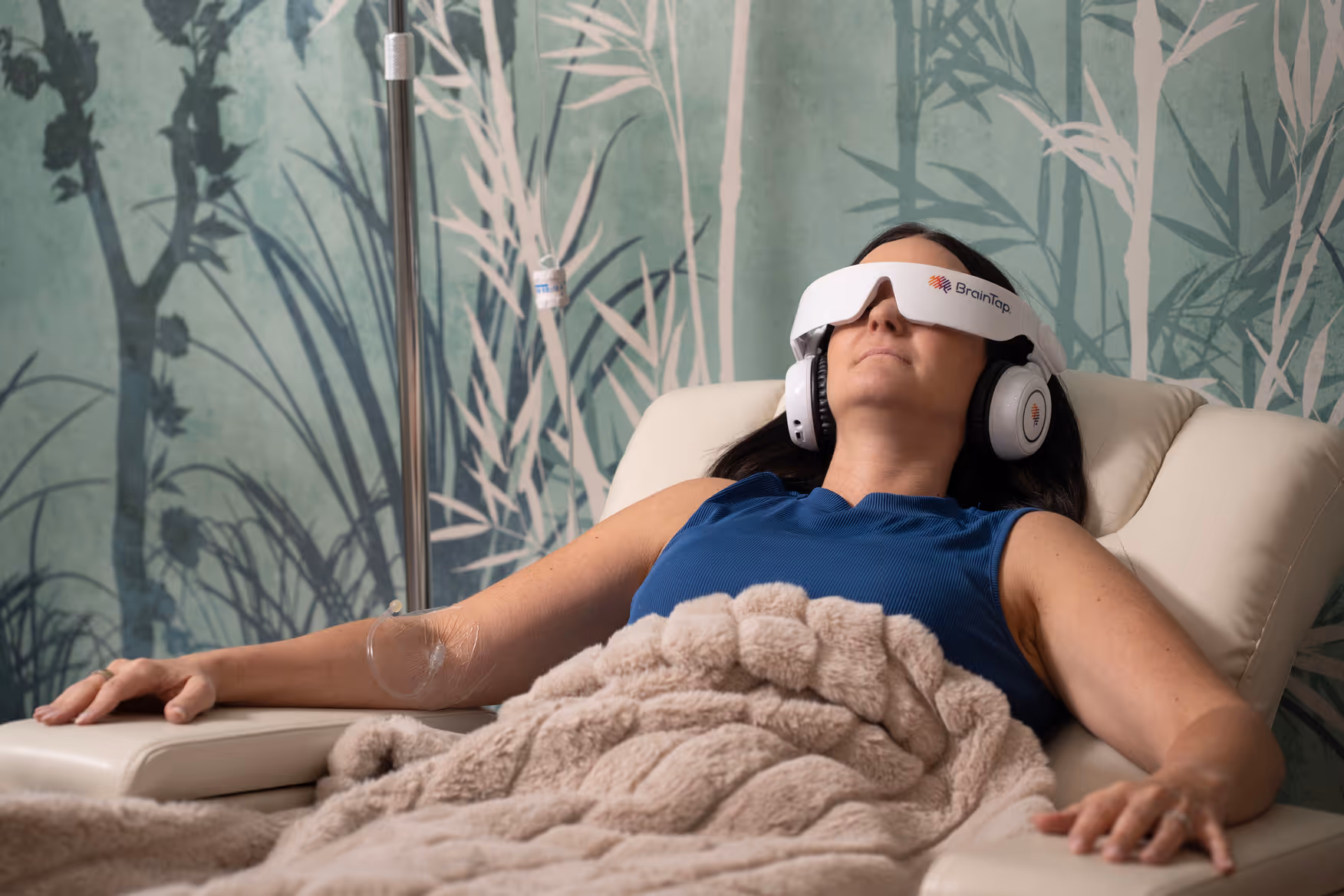 A patient reclining under a soft blanket with an eye mask and headphones during an infusion in the Nova IV Lounge
