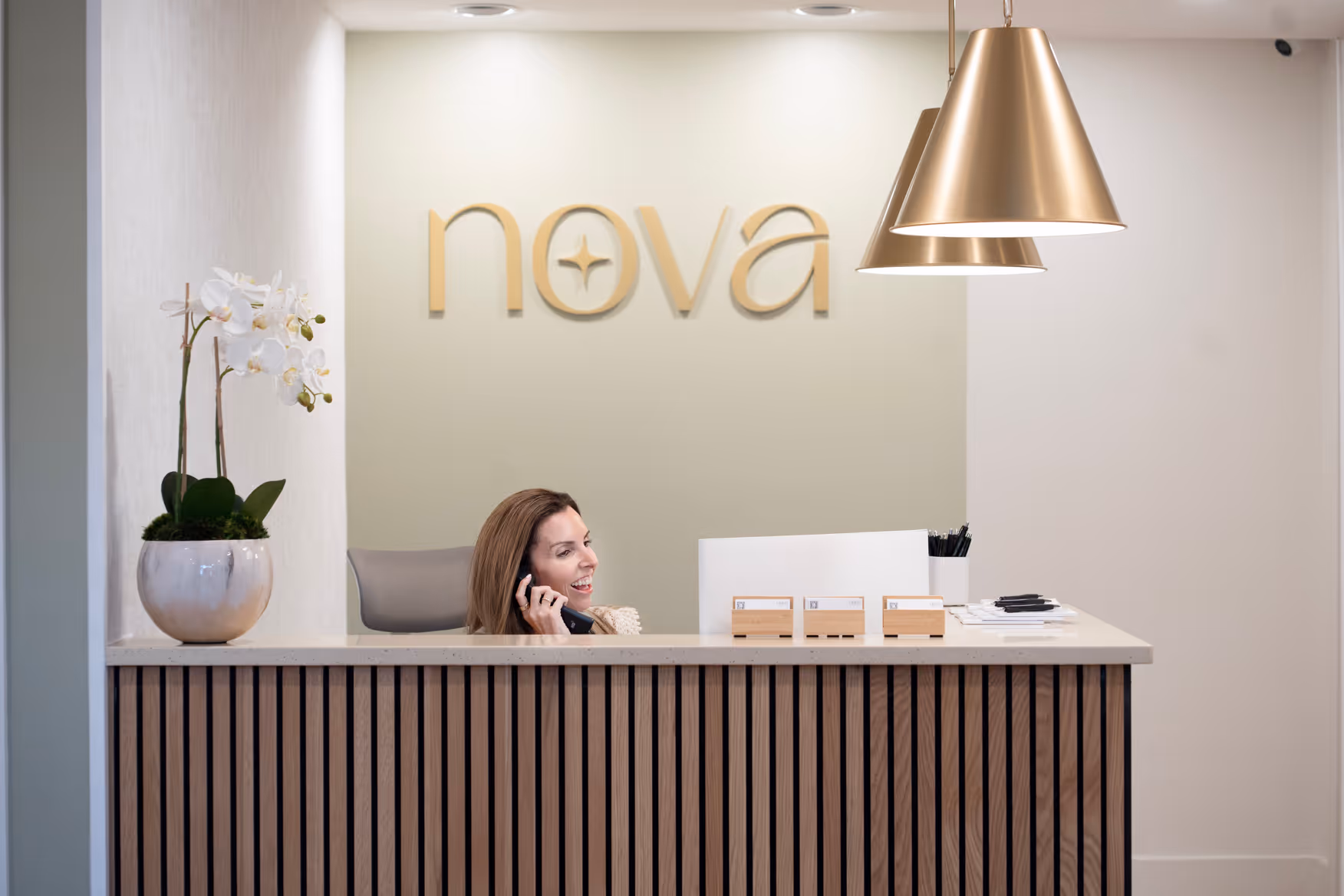 A Nova Wellness team member on the phone at the front desk beneath the gold Nova sign