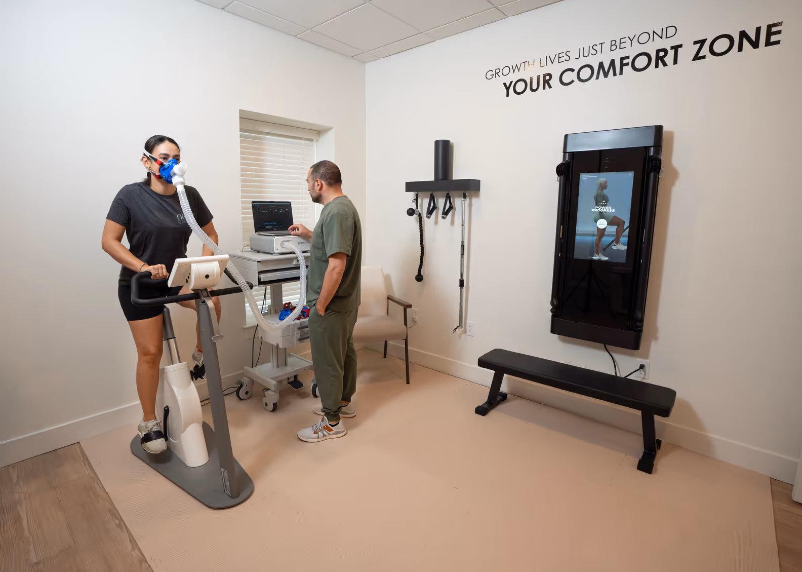 A patient on a stationary bike wearing a breathing mask for VO2 max testing as a clinician monitors the results